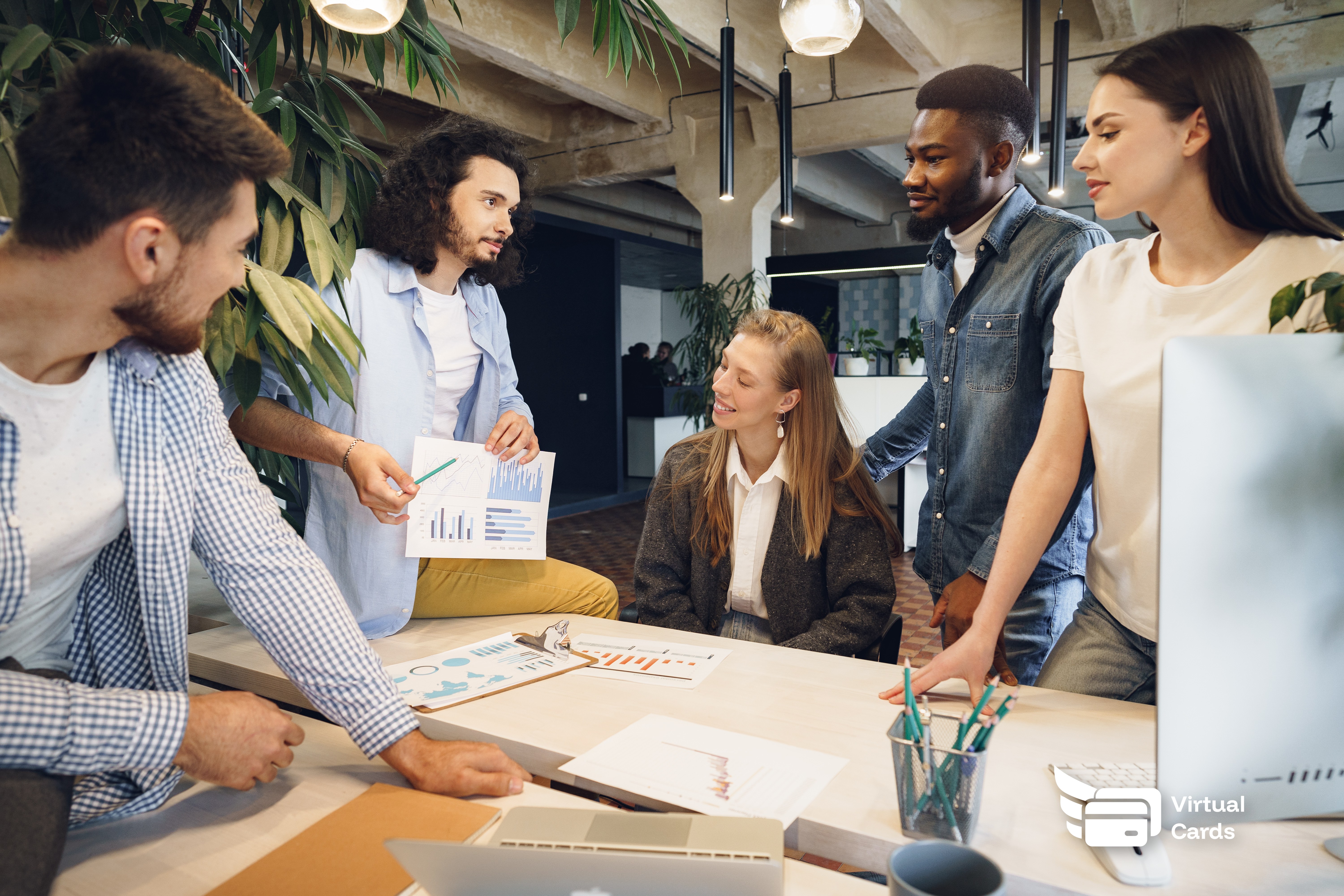 Diverse startup team reviewing company spending cards in a modern co-working office.